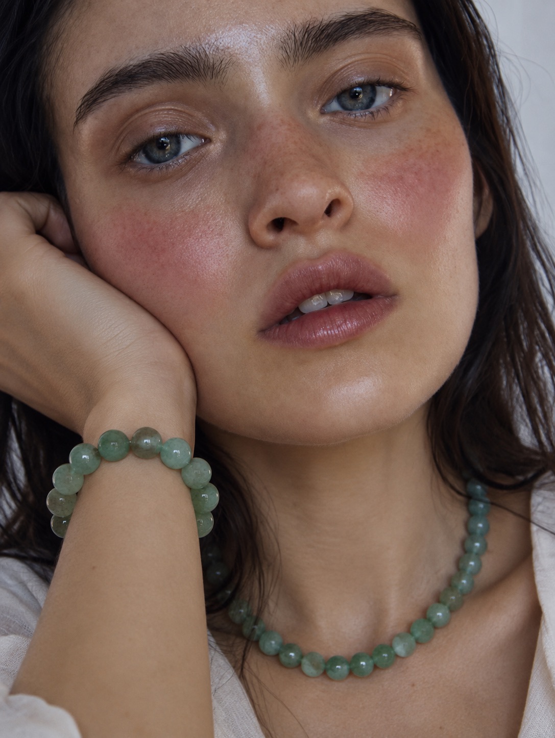 A woman wearing a green gemstone bead bracelet and matching necklace